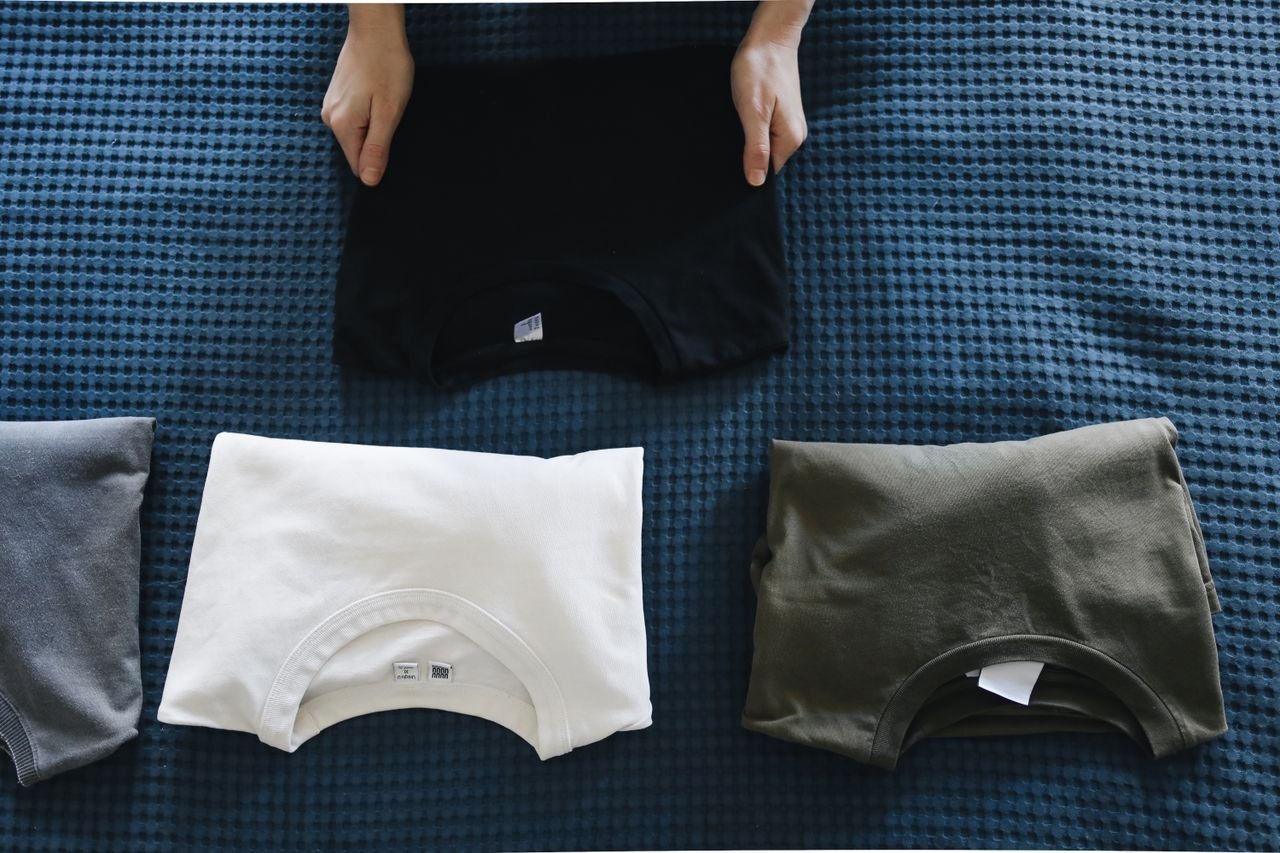 Home Top view of neatly folded colored T-shirts laid out on a blue bedspread, perfect for housekeeping themes.