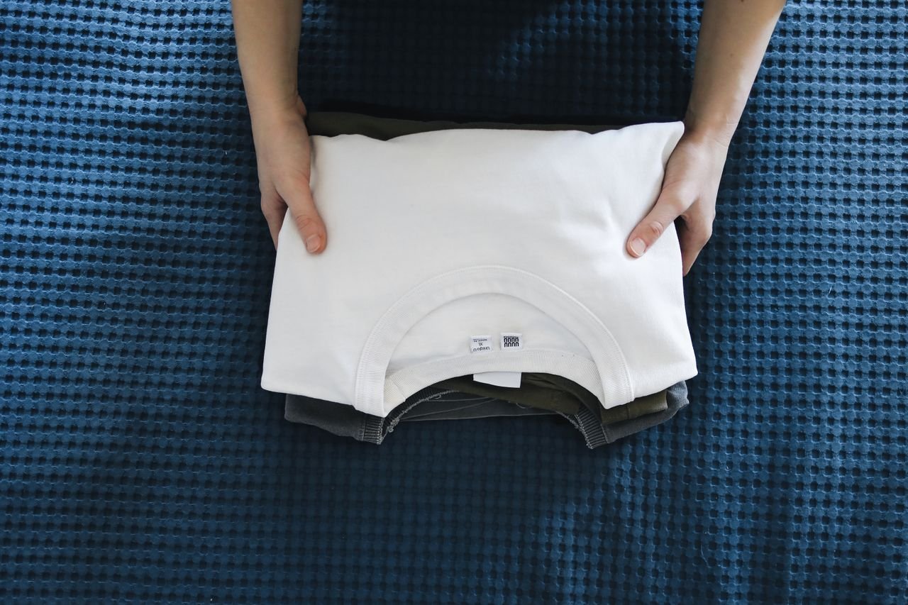 Home Hands folding a white shirt on a blue textured bedspread, focusing on organizing clothes.