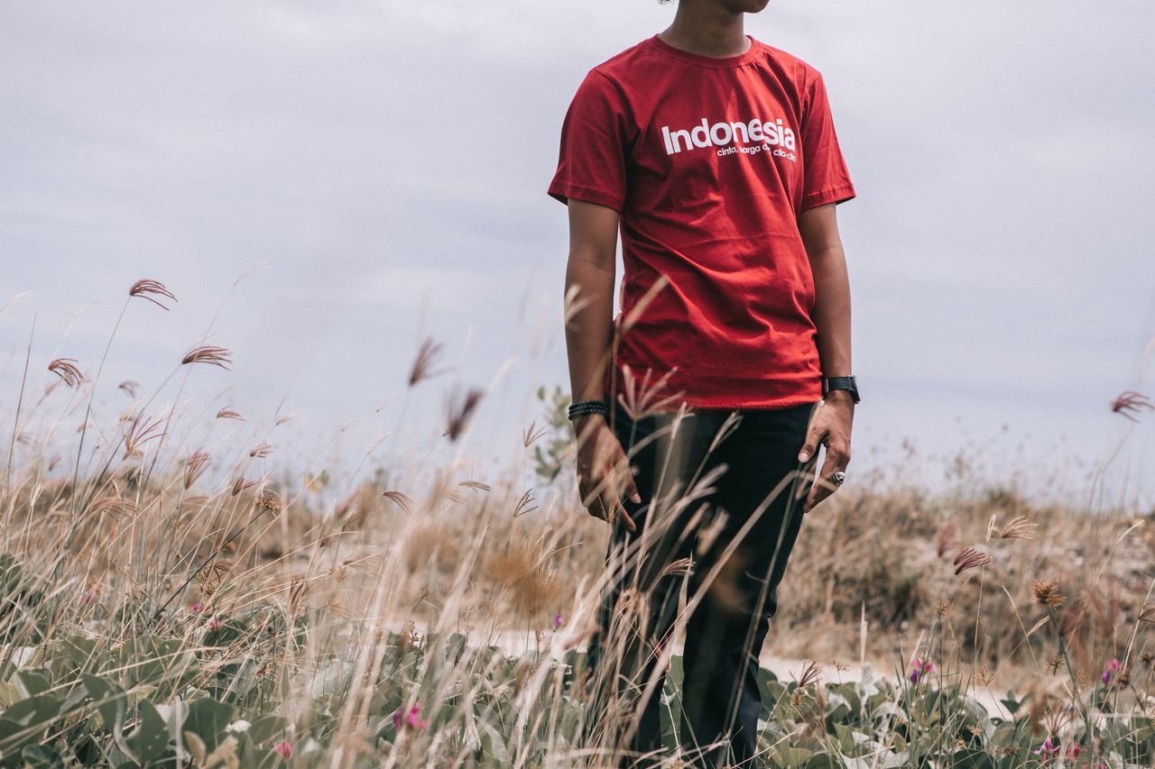 A man wearing a red Indonesia shirt stands in a grassy field in Bali.
